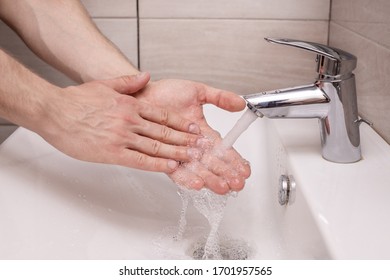 A man carefully washes his hands with water under the tap in the bathroom - Shutterstock ID 1701957565