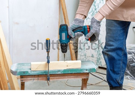 Man carpenter using electric drill to screw into timber wood block on workbench. Home renovation and furniture construction project. Professional woodworking service and handyman task concept