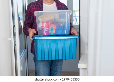 The man carries two plastic boxes with things, the upper transparent, the lower container is blue.