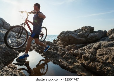 Man carrying a bike on the rock through water