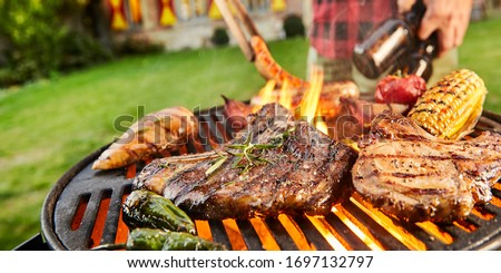 Man carrying bottles ob beer barbecuing outdoors in a close up view on assorted meat grilling over the flaming hot coals