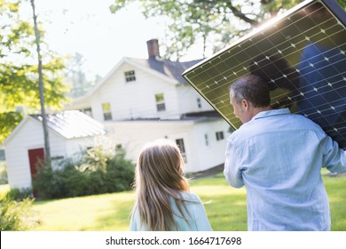 A man carrying a solar panel towards a building under construction. - Shutterstock ID 1664717698