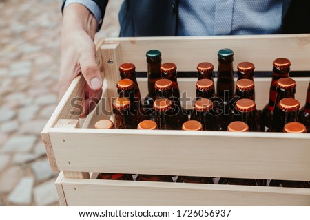 Man carrying wooden crate full of unmarked beverage bottles.