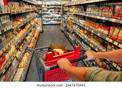 A man with a cart walks between store shelves and buys groceries. Large purchase at the supermarket. - Powered by Shutterstock