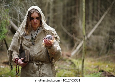 A man in a cassock spends a ritual in a dark forest with a crystal ball and book