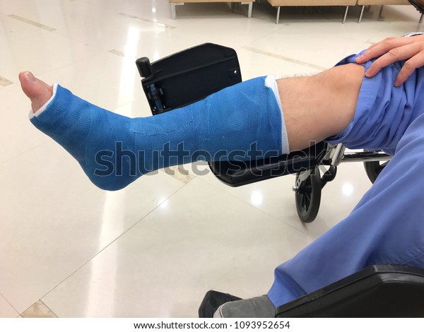 A man with cast around broken leg sitting on a\
wheelchair at the hospital.