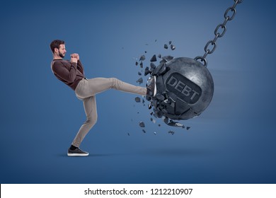 A Man In Casual Clothes Kicks A Giant Wrecking Ball With A Word DEBT Written On It. Debt Or Insurance. Getting Money Back. Rebuilding Your Fortune.