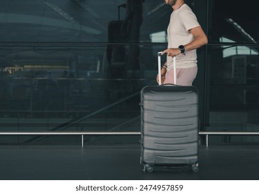 A man in casual clothing walks through an airport terminal with a large rolling suitcase - Powered by Shutterstock