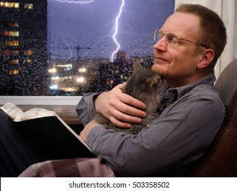 Man With A Cat And A Book In An Armchair. Outside, Night City, Rain, Storm