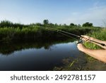 Man catching fish, pulling rod while fishing from lake or pond. Fisherman with rod, spinning reel on river bank. Sunrise. Fishing for pike, perch, carp on beach lake or pond. Background wild nature.