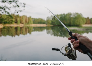 Man catching fish, pulling rod while fishing from lake or pond. Fisherman with rod, spinning reel on river bank. Sunrise. Fishing for pike, perch, carp on beach lake or pond. Background wild nature. - Shutterstock ID 2166035473