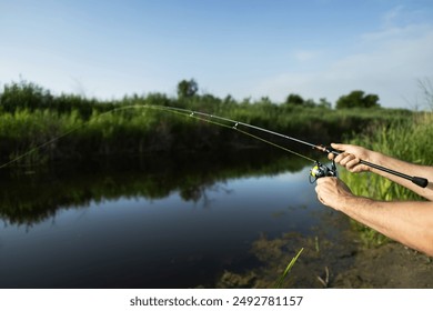 Man catching fish, pulling rod while fishing from lake or pond. Fisherman with rod, spinning reel on river bank. Sunrise. Fishing for pike, perch, carp on beach lake or pond. Background wild nature. - Powered by Shutterstock