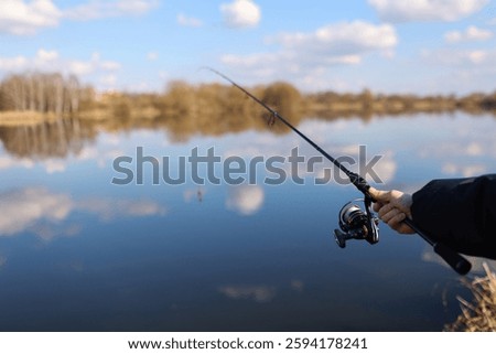 Man catching fish, pulling rod while fishing from lake or pond. Fisherman with rod, spinning reel on river bank. Fishing for pike, perch, carp on beach lake or pond. Wild nature, rural getaway
