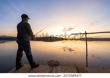 man catching fish in the river on the background sunset.