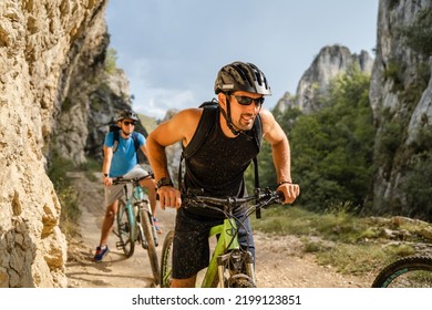 Man Caucasian Male Cyclist Riding E-bike Electric Bicycle Outdoor In Mountain Range At The Gorge Or Ridge In Front Of His Friends Wear Protective Helmet And Eyeglasses In Sunny Day Copy Space