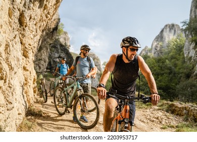 man caucasian male cyclist riding e-bike electric bicycle outdoor in mountain range at the gorge or ridge in front of his friends wear protective helmet and eyeglasses in sunny day copy space