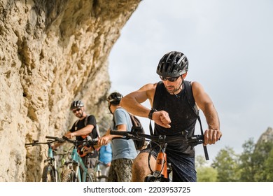 man caucasian male cyclist riding e-bike electric bicycle outdoor in mountain range at the gorge or ridge in front of his friends wear protective helmet and eyeglasses in sunny day copy space