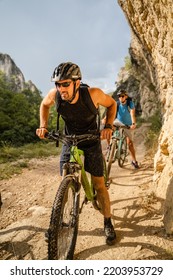 Man Caucasian Male Cyclist Riding E-bike Electric Bicycle Outdoor In Mountain Range At The Gorge Or Ridge In Front Of His Friends Wear Protective Helmet And Eyeglasses In Sunny Day Copy Space