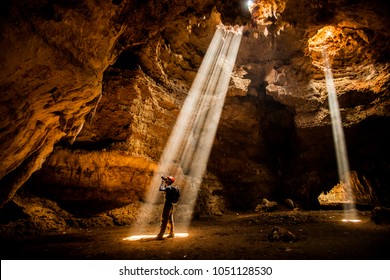 Man in the cave exploration with Ray of light - Shutterstock ID 1051128530