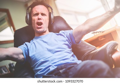 A Man Celebrating A Goal While Listening To His Favourite Team On Wireless Headphones In A Relaxing Armchair. 