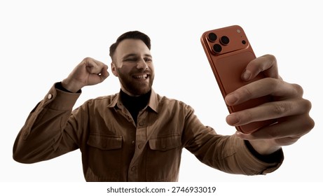 Man celebrating while looking at smartphone isolated on white background. Concept of online profit, stock trading success, crypto growth, fintech app notification and digital financial achievement.