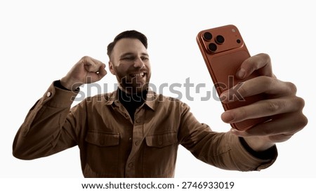 Man celebrating while looking at smartphone isolated on white background. Concept of online profit, stock trading success, crypto growth, fintech app notification and digital financial achievement.