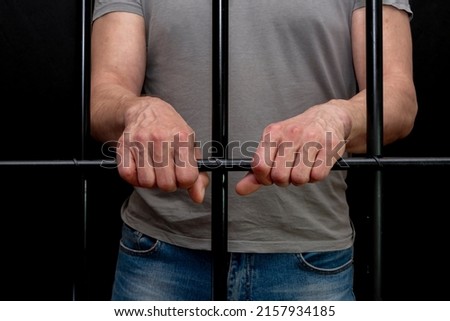 The man in the cell put his hands on the bars. Concept: a prisoner in a courtroom, a court sentence to a convicted person, a prison term.