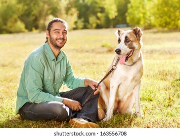 Man And Central Asian Shepherd Walk In The Park. He Keeps The Dog On The Leash.