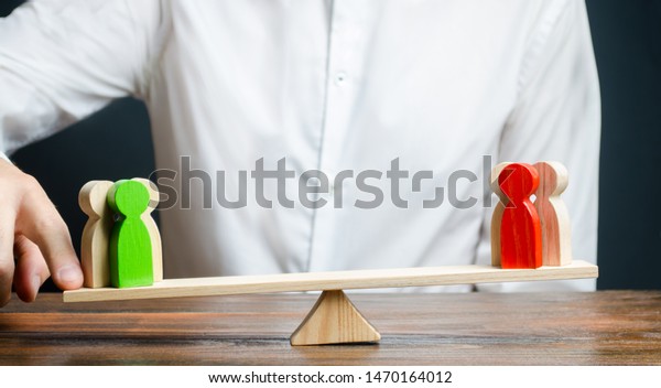 A man changes the balance of scales in favor of a\
green group of people. Mediator services. Conflict, dispute\
resolution, judicial system. Negotiations and decision making in\
favor of one of the sides