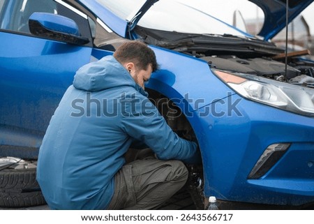 A man changes the brake fluid in a blue car