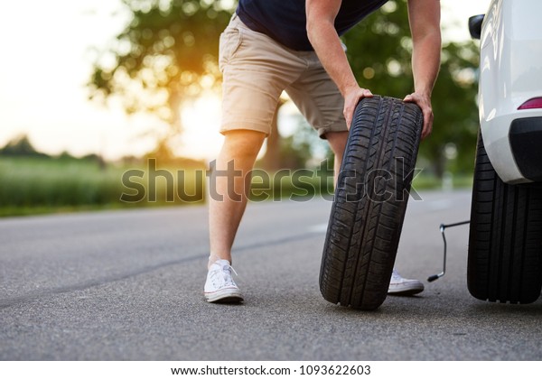 The man\
changes the tire to a broken car on the\
road