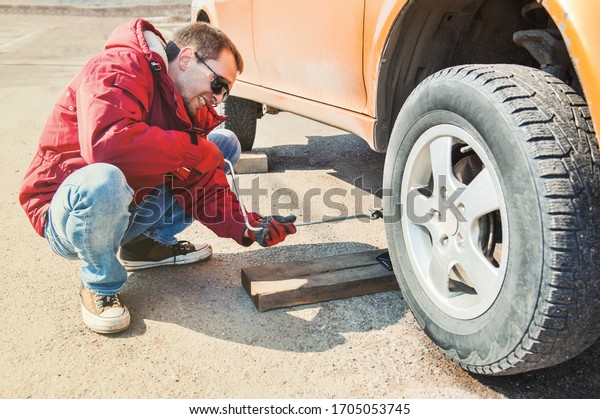 a man changes wheels on a car. exit tire service.\
unscrews the wheel nuts with a wrench. car service. lifts the car\
with a jack