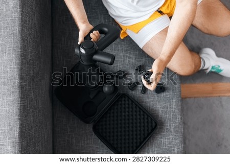 Man changing attachments on a percussion massage gun for post-workout recovery. The massage gun supports post-workout recovery while helping with myofascial release during self-care and rehabilitation. This high-quality photo shows massage gun accessories, post-workout recovery, and myofascial release for muscle treatment and relaxation.
