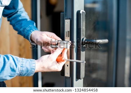Man changing core of a door lock of the entrance glass door, close-up view with no face