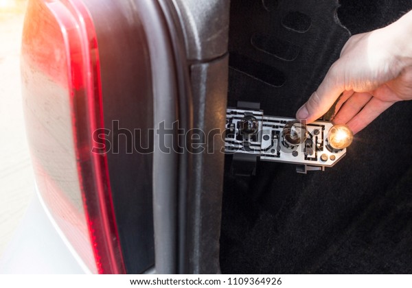 A man is changing a light bulb in the rear of\
the car, close-up