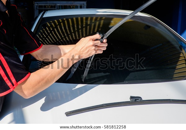 Man is changing\
windscreen wipers on a car, Asian man installing new windshield\
wipers by himself at home