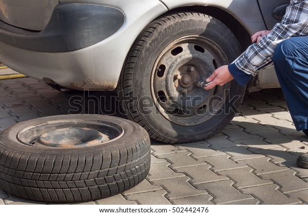 Man is changing\
winter tire with wheel wrench. Preparing the car for the winter.\
Repairing punctured\
tires.\
