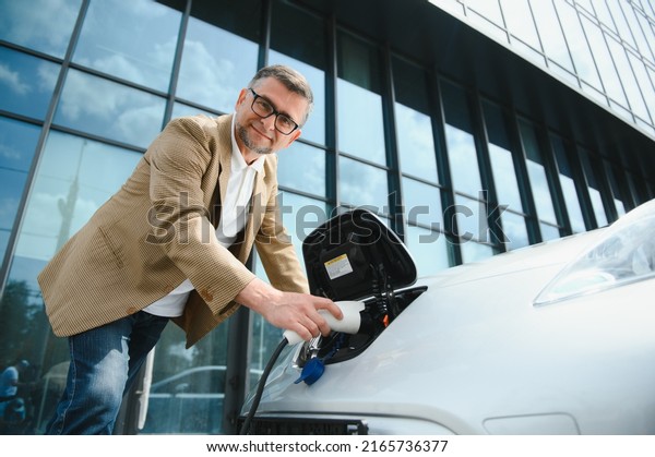 Man\
charges an electric car at the charging\
station.