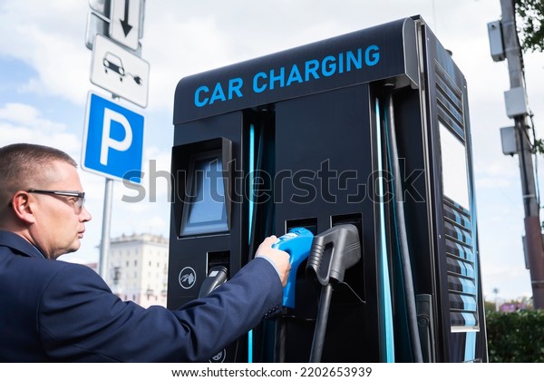 Man charges an electric car at the\
charging station. electric car battery charging station on a city\
street. A modern gas station with\
electricity.