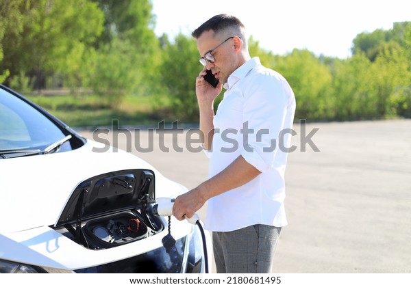 a\
man charges an electric car and talks on a mobile\
phone