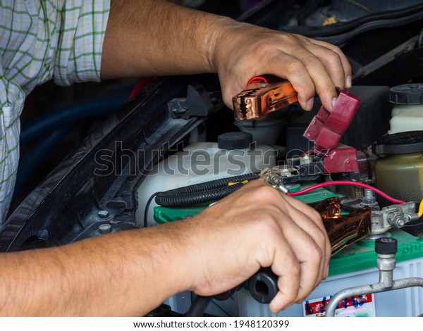 A man charging battery car with\
electricity trough jumper cables,service\
concept.