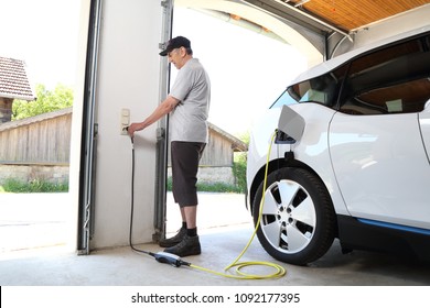 A Man Charging Electric Car  At Outlet At Home