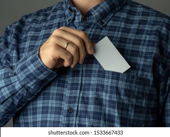 A Man In A Checked Blue Shirt Tucks A Business Card Into His Shirt Pocket.