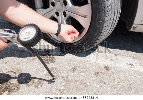 Man checking air pressure in a car tire using an air\
pressure gauge 