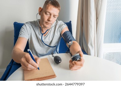 Man checking blood pressure manually with sphygmomanometer and stethoscope and writing down results in notebook. Manual blood pressure measurement and tracking. Responsibility in health