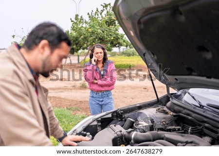 Man checking car engine while woman calls for assistance on a road trip after experiencing vehicle malfunction