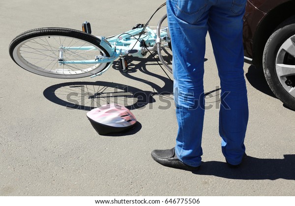 Man checking consequences of car and bicycle\
accident on street