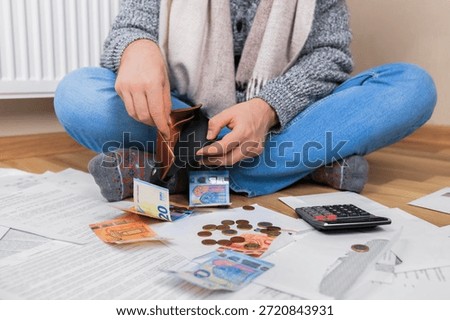 Man checking empty wallet sitting on floor near radiator with bills and money, struggling with heating costs and debt. High quality photo