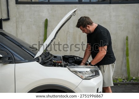 Man checking the engine of a broken car with the hood open. Vehicle breakdown and repair concept, driver inspecting engine after mechanical problem.