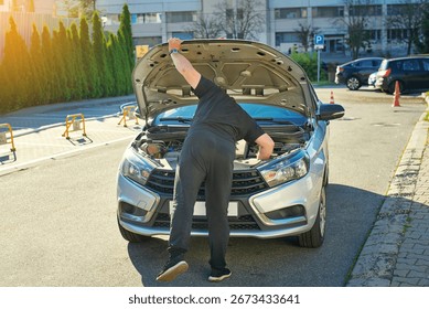 Man checking engine under open hood of silver car, vehicle repair, troubleshooting, and automobile maintenance work. Driver checking under hood of car during vehicle breakdown, problem solving